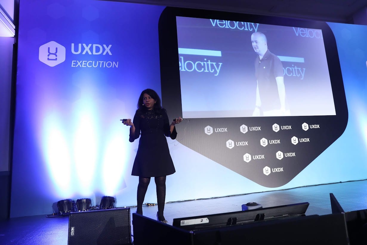 A speaker is on the UXDX stage at an EMEA conference in Dublin, Ireland.